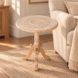 May include: A round wooden side table featuring a light brown finish with white-washed floral carvings on the tabletop and central pedestal. The table stands on three curved legs and includes a small central support post with decorative details.