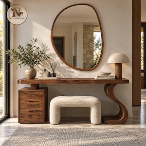 May include: A wooden console table with a three-drawer cabinet on the left and a curved support on the right. It features a cream-colored textured bench, a large organic-shaped wall mirror, a table lamp, and a vase with green foliage.
