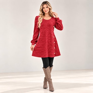 May include: A long-sleeved red tunic dress with a heathered texture, featuring a round neckline and a vertical row of light-colored buttons running down the left side. The dress is paired with black leggings and tall tan suede boots.
