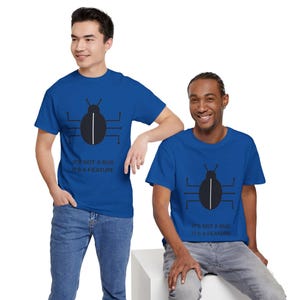Könnte beinhalten: Ein königsblaues Kurzarm-T-Shirt mit einer schwarzen Grafik eines stilisierten Käfers mit schaltkreisartigen Beinen und einer weißen vertikalen Linie in der Mitte. Unter der Grafik steht der Text: IT'S NOT A BUG IT'S A FEATURE in Schwarz.