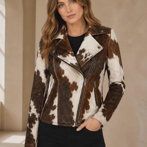 May include: A moto-style jacket featuring a brown and white cowhide print pattern. The jacket has a notched lapel, an asymmetrical front zipper closure, and two zippered pockets on the front. The sleeves are long and the fit is tailored.