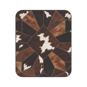 May include: A rectangular throw blanket featuring a patchwork design of cowhide panels in shades of brown, black, and white. The individual pieces are joined together with visible white stitching, creating a geometric star-like pattern.