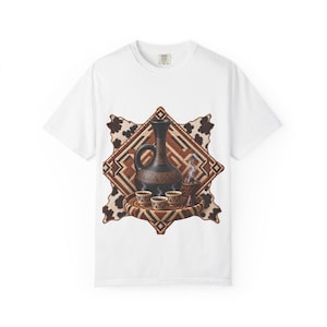 May include: A white short-sleeved t-shirt featuring a graphic print of a black coffee pot, three small cups, and an incense burner on a woven tray, set against a brown geometric pattern and a black and white cowhide-style background.