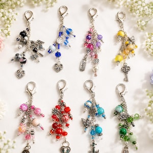 May include: Eight silver-toned metal lobster clasp keychains, each featuring a unique arrangement of colorful beads and charms. The charms include hearts, keys, butterflies, flowers, and anchors, with beads in black, blue, pink, yellow, red, and green.