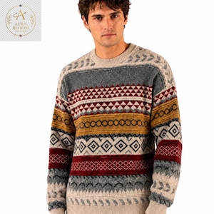 May include: A crew neck sweater featuring a horizontal pattern of geometric shapes in shades of gray, cream, mustard yellow, and deep red. The knit garment displays repeating triangles, diamonds, and linear bands across the chest and sleeves.