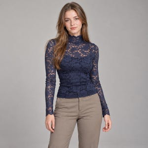 Puede incluir: Una blusa de encaje azul marino de manga larga con cuello alto y corte ajustado. La prenda presenta un delicado patrón de encaje floral que se extiende por las mangas y el cuerpo, combinada con pantalones de color caqui liso.