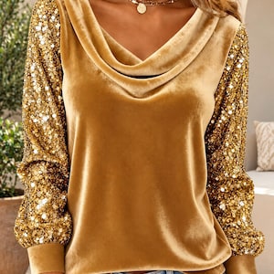 May include: A long-sleeve top featuring a gold velvet bodice with a cowl neckline and contrasting gold sequined sleeves. The garment has fitted velvet cuffs at the wrists and is paired with light blue denim jeans, creating a textured appearance.