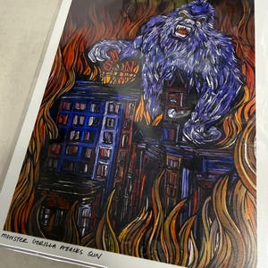 May include: A print featuring a purple gorilla attacking a city engulfed in flames. The artwork includes the text "MONSTER GORILLA ATTACKS SUN" and a stylized depiction of a building with the word "SUN" on top.