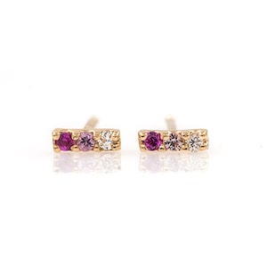 May include: A pair of gold earrings with three small gemstones each. The gemstones are pink, purple, and white.