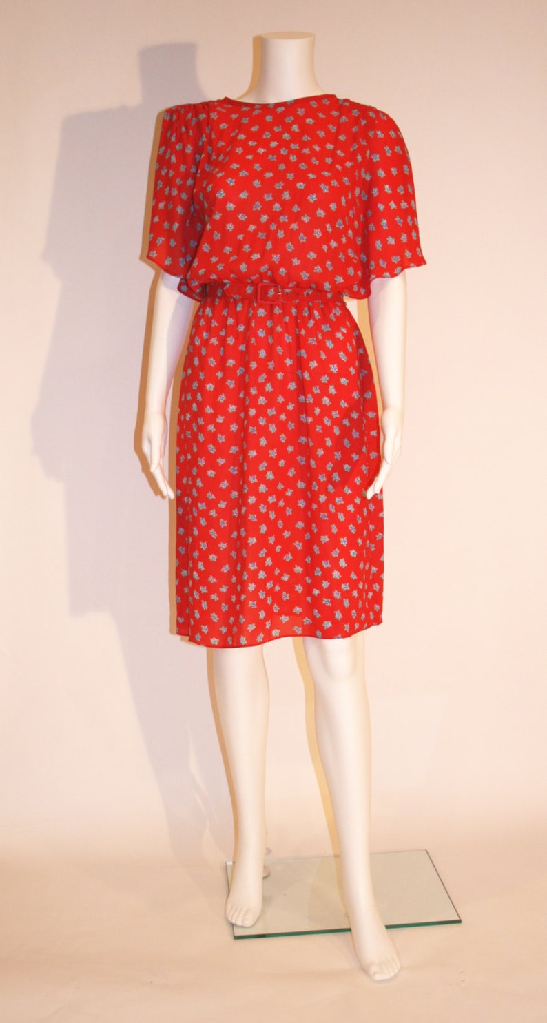 May include: A red dress with a small blue floral pattern. The dress has a gathered waist and short sleeves.