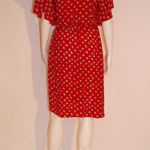 May include: A red dress with a white floral pattern. The dress has short, puffed sleeves and a fitted bodice. The dress is knee-length and has a gathered skirt.