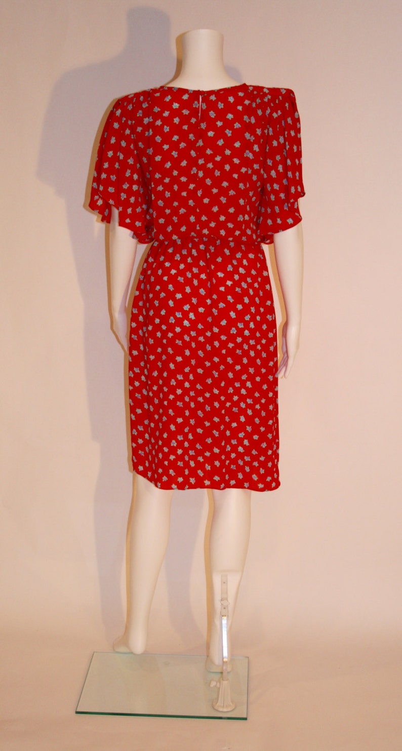 May include: A red dress with a white floral pattern. The dress has short, puffed sleeves and a fitted bodice. The dress is knee-length and has a gathered skirt.