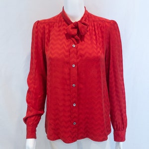 May include: A red long-sleeved blouse with a chevron pattern and a bow tie at the neck.