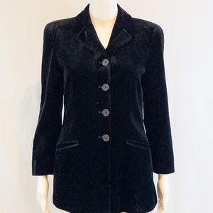 May include: A black velvet blazer with a notched collar and three-button closure. The blazer has two front pockets and long sleeves. The garment is displayed on a mannequin.
