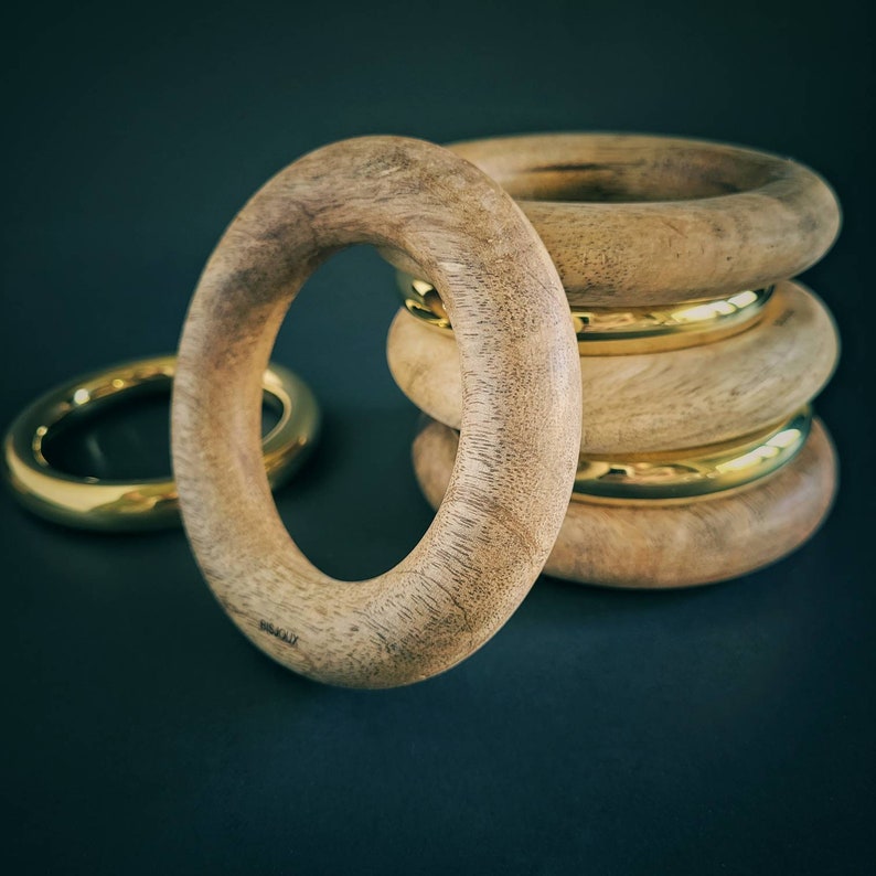 May include: A set of four wooden bangles with gold accents. The bangles are stacked on top of each other, with the largest bangle at the bottom and the smallest bangle at the top.