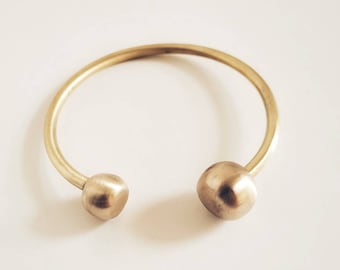 May include: A gold-toned bangle bracelet with two round, smooth, ball-shaped ends.