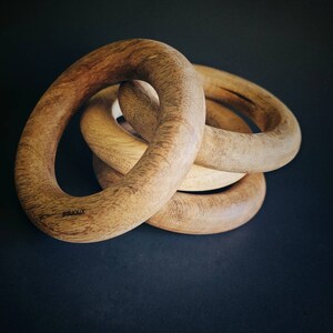 May include: Four wooden rings interlocked together, with the text "BISOUX" engraved on the largest ring.