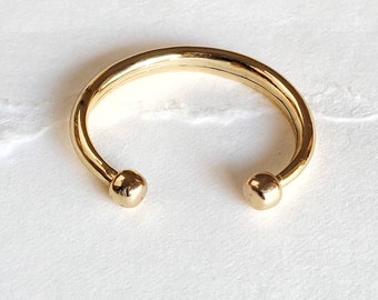 May include: A gold-toned bangle bracelet with rounded ends. The bracelet is made of a thick, smooth metal.