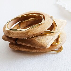 May include: A set of four wooden bangles with gold metal accents. The bangles are stacked on top of each other, with the largest bangle at the bottom and the smallest bangle at the top.