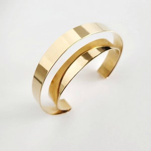 May include: A gold-toned bangle bracelet with a double band design. The bracelet is made of two thin bands of metal that are joined together at the ends.