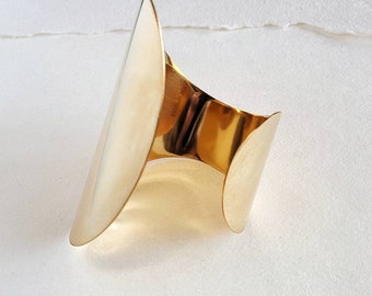 May include: A gold metal cuff bracelet with a unique, curved design. The bracelet is open on one side and has a smooth, polished finish.