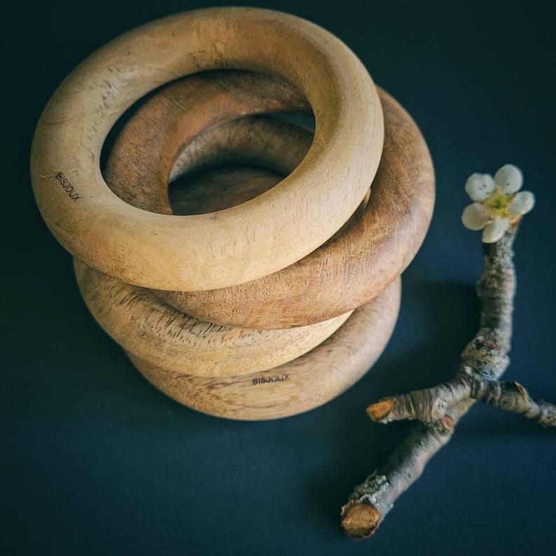May include: Four wooden rings stacked on top of each other. The rings are all different sizes and have a natural wood finish. The rings are engraved with the word "Bijoux".