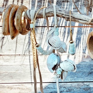 May include: A set of gold tone necklaces with a variety of charms, including seashells and beads. The necklaces are hanging from a wooden branch.