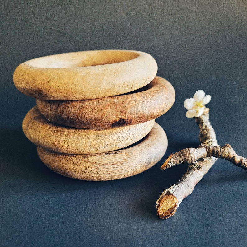 May include: Four wooden bowls stacked on top of each other. The bowls are made of light brown wood and have a smooth, rounded surface. The bowls are arranged in a staggered pattern, with the largest bowl at the bottom and the smallest bowl at the top. A small branch with a white flower is in the background.