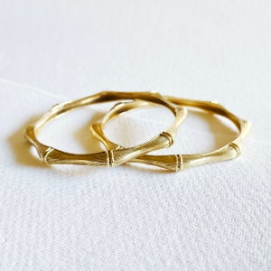 Op de afbeelding: Twee gouden armbanden met een bamboe-achtig ontwerp.