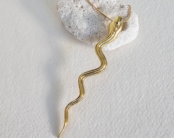 May include: A gold snake pendant necklace with a textured, wavy design. The pendant is hanging from a thin gold chain.
