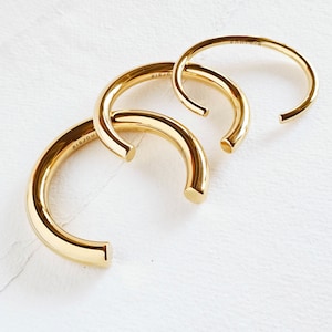 Op de afbeelding: Drie gouden metalen armbanden met het woord "BISJOUX" gegraveerd op een van de armbanden.