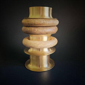 May include: A stack of three wooden rings with a gold metal base. The rings are made of natural wood and have a smooth finish. The base is a simple, round shape.