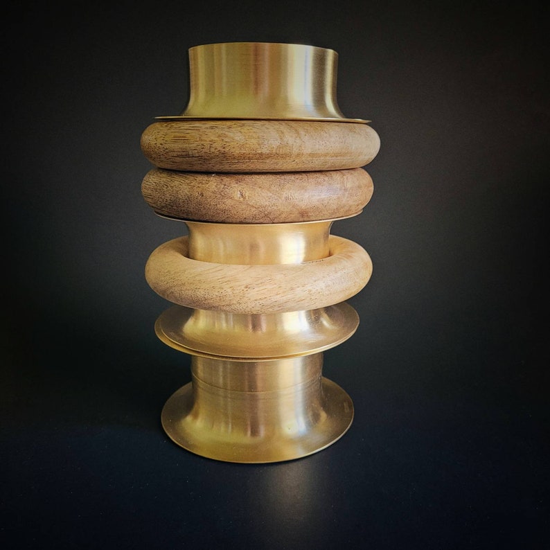 May include: A stack of three wooden rings with a gold metal base. The rings are made of natural wood and have a smooth finish. The base is a simple, round shape.