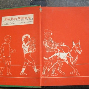 May include: A red book with a green border. The front cover features an illustration of three children and a dog. The back cover has a handwritten inscription that reads "This Book Belongs to Dick No 7 New Haven Conn Callahan 1943-1944."