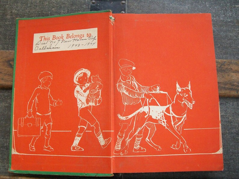 May include: A red book with a green border. The front cover features an illustration of three children and a dog. The back cover has a handwritten inscription that reads "This Book Belongs to Dick No 7 New Haven Conn Callahan 1943-1944."