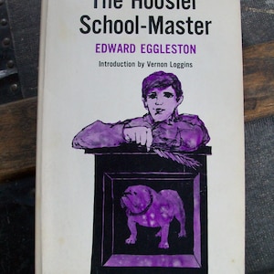 May include: A vintage paperback book cover with a purple illustration of a man leaning on a podium with a bulldog in a frame. The book title is "The Hoosier School-Master" by Edward Eggleston. The book is part of the American Century Series and costs $1.50.