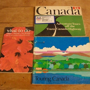 May include: Three vintage travel guide books with colorful covers. The top book is red, white, and blue with the word "Canada" in large white letters. The middle book is red with a large pink hibiscus flower. The bottom book is blue with a scenic landscape of mountains, trees, and a lake. The text on the bottom book reads "Touring Canada".