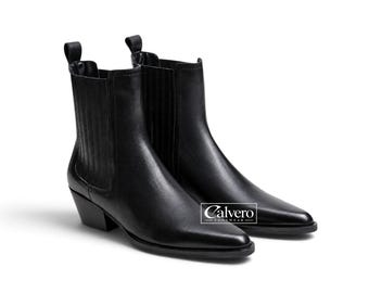 May include: A pair of black leather Chelsea boots with pointed toes, stacked heels, and elastic side panels. A pull tab is located at the back of each ankle. The text Calvero Footwear is printed in white on a rectangular black background.