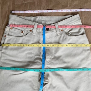 May include: A pair of light beige jeans with a measuring tape across the front and waist. The tape measures the waist at 30 inches and the inseam at 32 inches.
