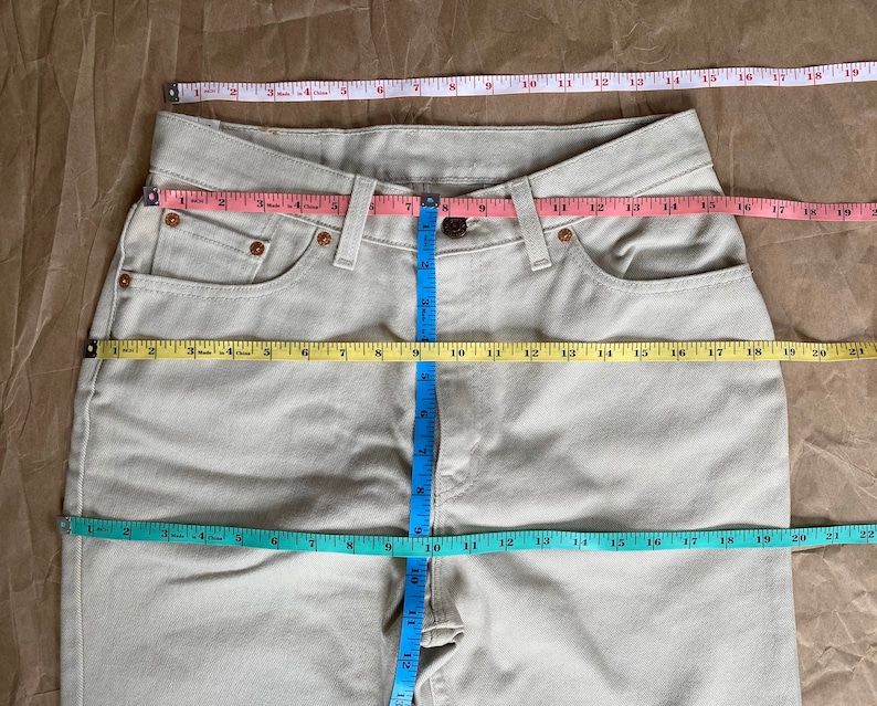 May include: A pair of light beige jeans with a measuring tape across the front and waist. The tape measures the waist at 30 inches and the inseam at 32 inches.