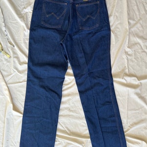 K&ouml;nnte beinhalten: Dunkelblaue Wrangler Jeans mit hohem Bund und geradem Bein. Die Ges&auml;&szlig;taschen haben eine W-f&ouml;rmige Naht. Das Wrangler-Etikett ist sichtbar. Die Jeans ist neu mit Etikett.