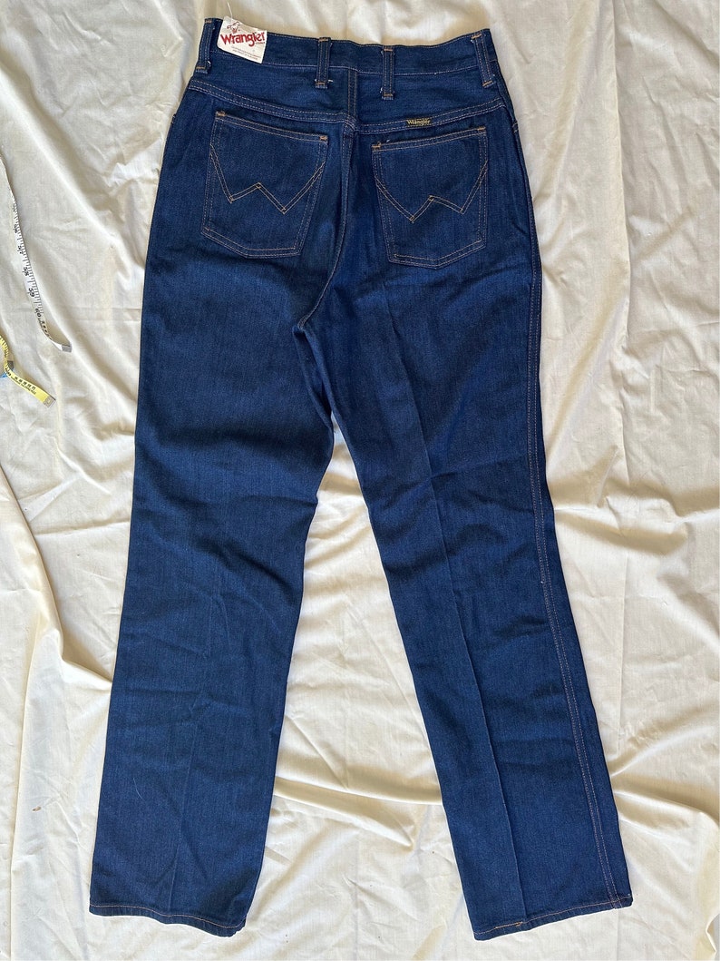 K&ouml;nnte beinhalten: Dunkelblaue Wrangler Jeans mit hohem Bund und geradem Bein. Die Ges&auml;&szlig;taschen haben eine W-f&ouml;rmige Naht. Das Wrangler-Etikett ist sichtbar. Die Jeans ist neu mit Etikett.