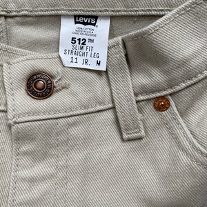 May include: A pair of light beige Levi's 512 Slim Fit Straight Leg jeans with a brown button and a Levi's tag that reads "512 TM Slim Fit Straight Leg 11 JR. M".