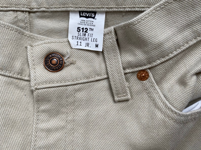 May include: A pair of light beige Levi's 512 Slim Fit Straight Leg jeans with a brown button and a Levi's tag that reads "512 TM Slim Fit Straight Leg 11 JR. M".