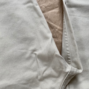 May include: Close-up of a pair of light beige denim jeans. The fabric has a subtle texture and the seams are visible.