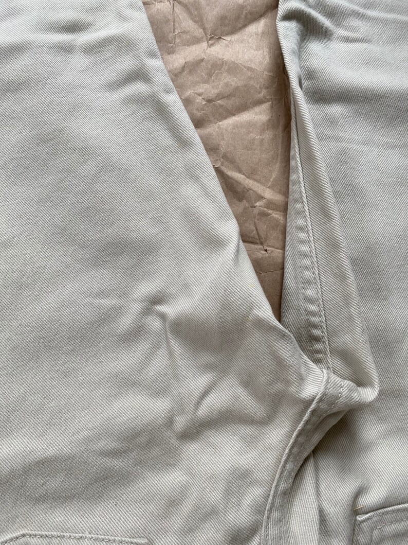 May include: Close-up of a pair of light beige denim jeans. The fabric has a subtle texture and the seams are visible.