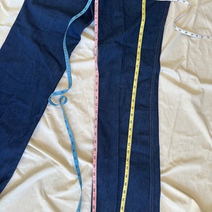 K&ouml;nnte beinhalten: Dunkelblaue Jeans mit geradem Bein. Mehrere Ma&szlig;b&auml;nder werden verwendet, um die Jeans zu messen. Die Innenbeinl&auml;nge misst ca. 76 cm. Die Jeans haben ein klassisches F&uuml;nf-Taschen-Design.
