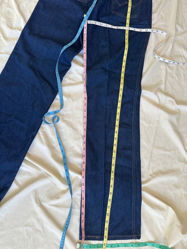 K&ouml;nnte beinhalten: Dunkelblaue Jeans mit geradem Bein. Mehrere Ma&szlig;b&auml;nder werden verwendet, um die Jeans zu messen. Die Innenbeinl&auml;nge misst ca. 76 cm. Die Jeans haben ein klassisches F&uuml;nf-Taschen-Design.