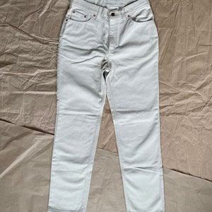 May include: A pair of light beige straight-leg jeans. The jeans have a classic five-pocket design and a button fly.
