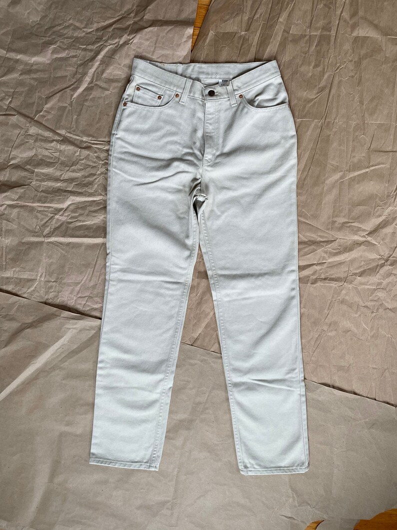 May include: A pair of light beige straight-leg jeans. The jeans have a classic five-pocket design and a button fly.